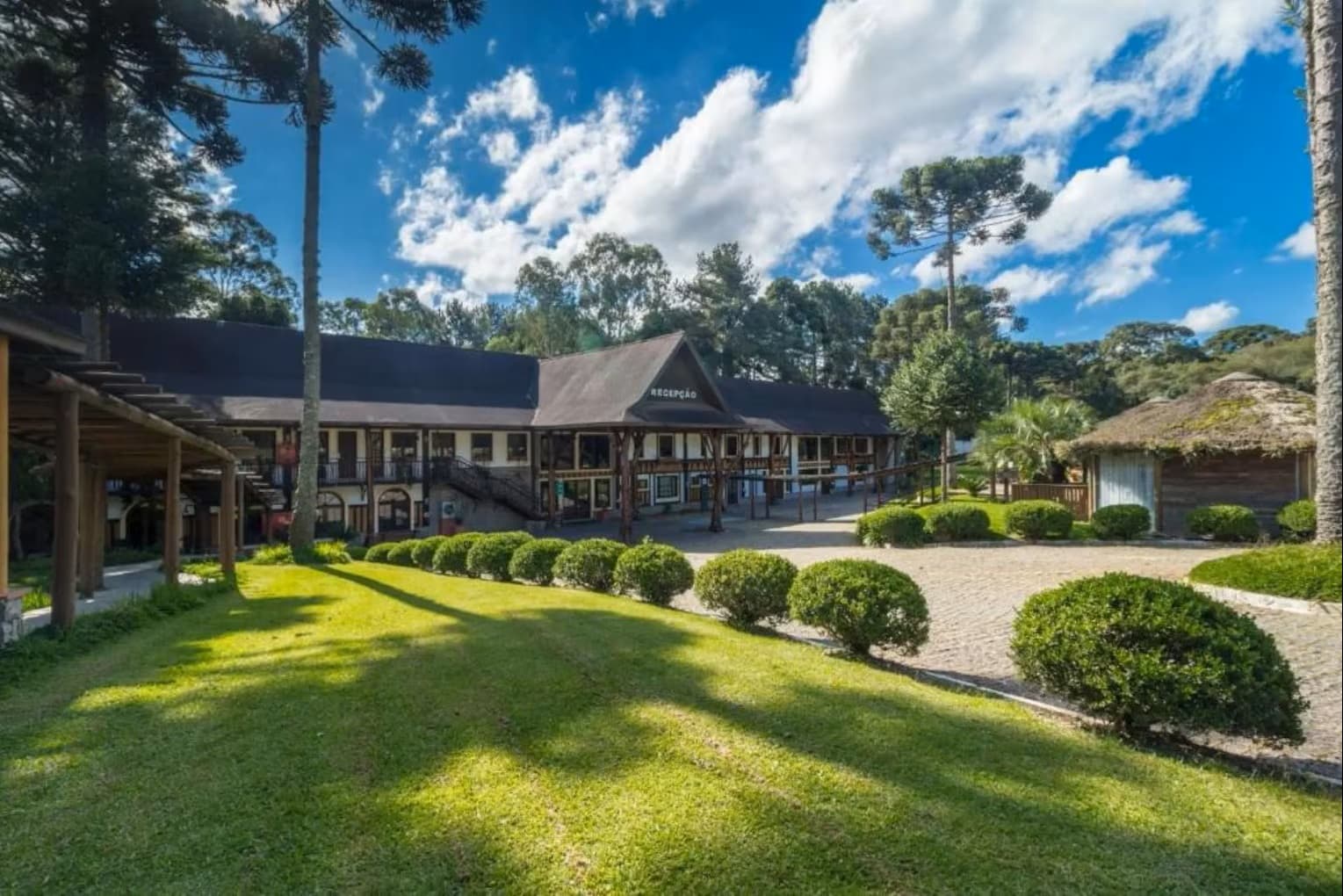 Fachada do La Dolce Vita Park Hotel, com a recepção, o gramado e as araucárias